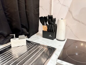 A kitchen with a stainless steel sink, a black knife block, and a paper towel holder. - Modern 2 Bedroom Flat in Luton Town Centre (Luton)