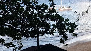 A beach with a boat in the water, a tree in the foreground, and a sandy shore. - Turquoise Sea Villa (Montego Bay)