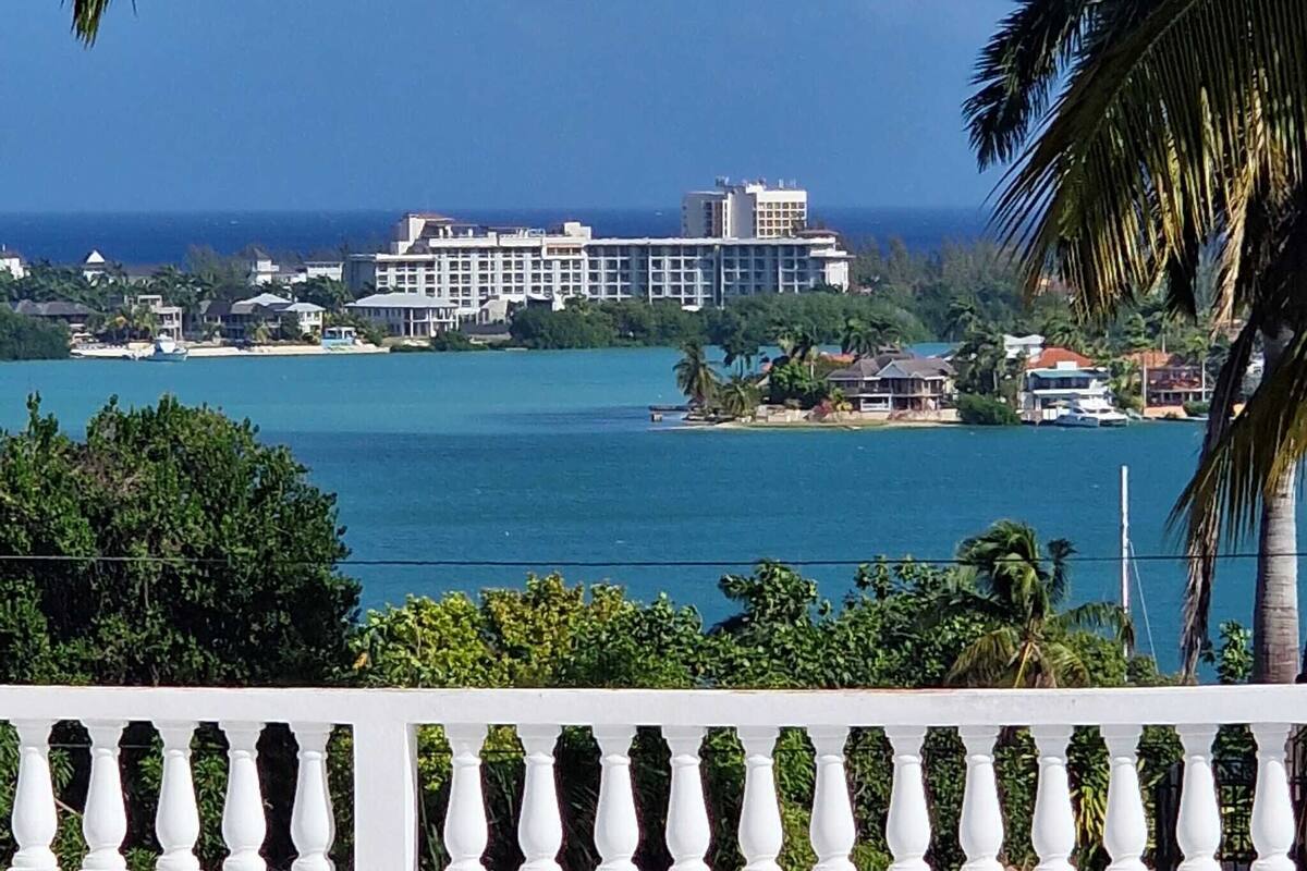 A coastal view with a large hotel building, palm trees, and a clear blue sky.