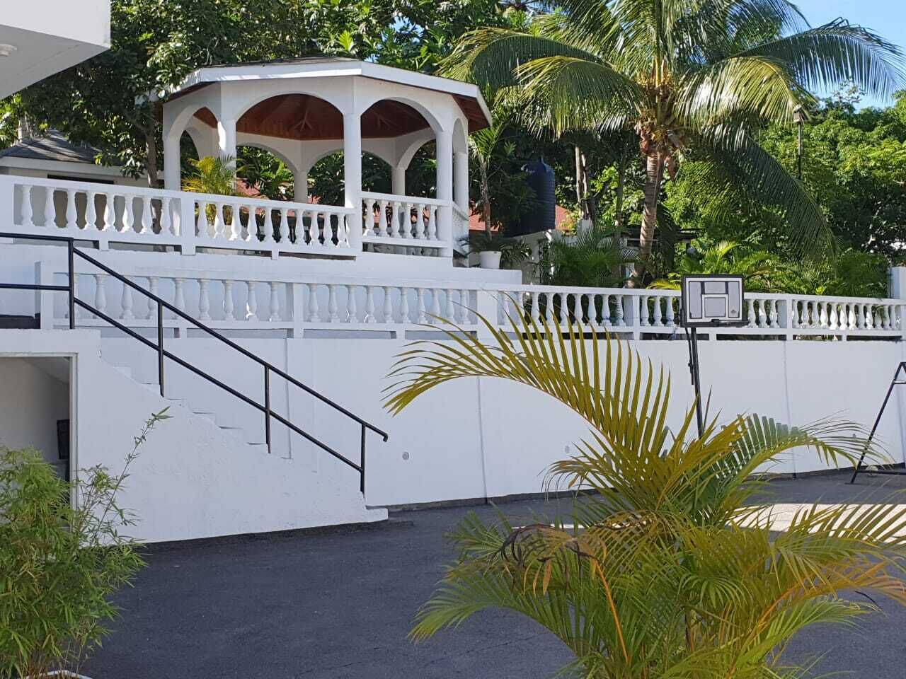 A white building with a covered outdoor area, a staircase, and a white fence.