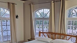 A bedroom with a large bed, wooden headboard, and two windows with curtains. - Turquoise Sea Villa (Montego Bay)