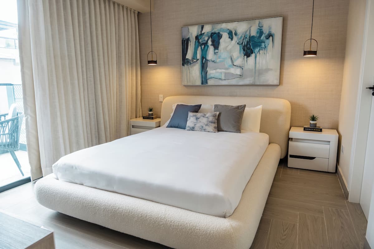 Una habitación de hotel moderna con una cama grande, dos mesitas de noche, un cuadro en la pared y vistas al exterior.