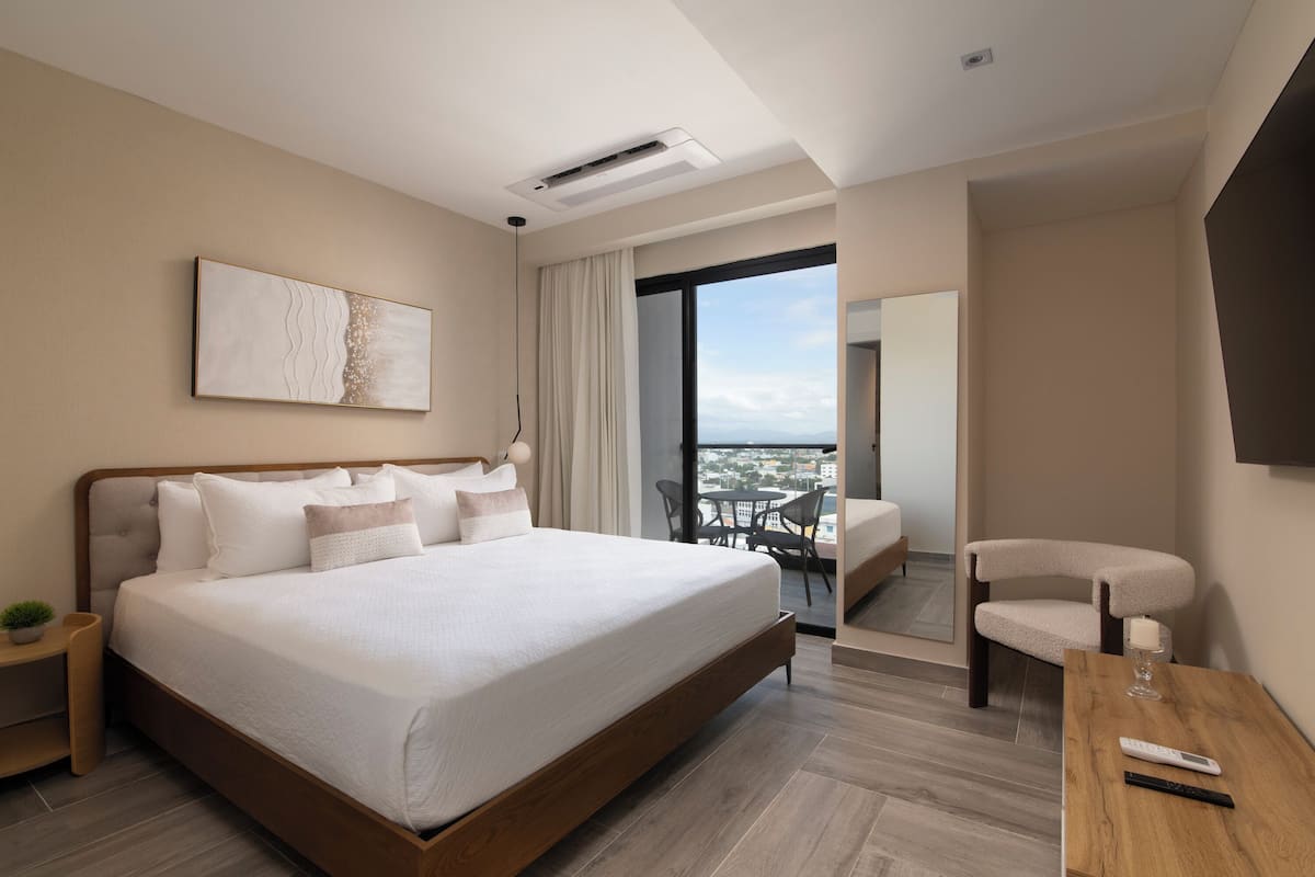 Una habitación de hotel moderna con una cama grande, una mesita, una silla y vistas a la ciudad.