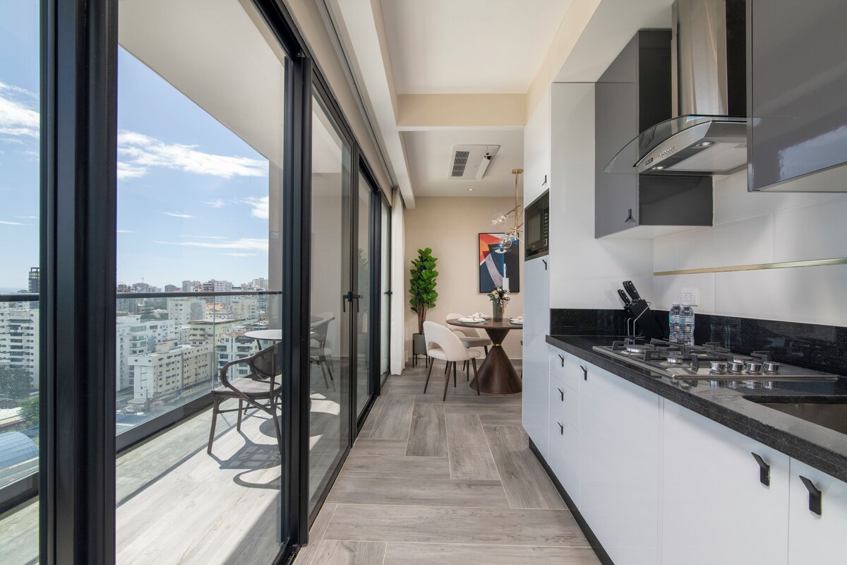 Une cuisine moderne dotée d’une grande fenêtre, d’un coin repas avec des chaises et offrant une vue sur le paysage urbain.