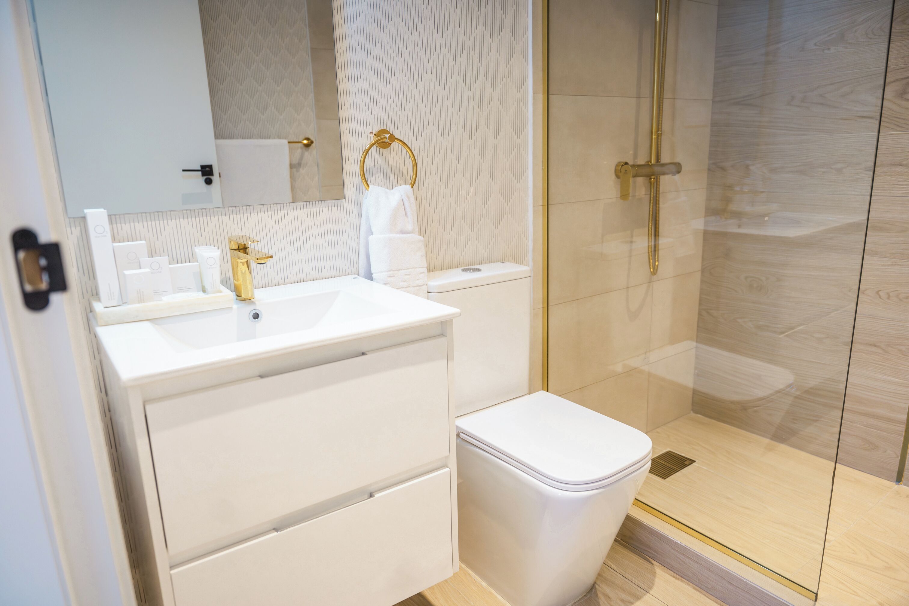 A modern bathroom with a white vanity, a gold faucet, a glass shower enclosure, and a white toilet.