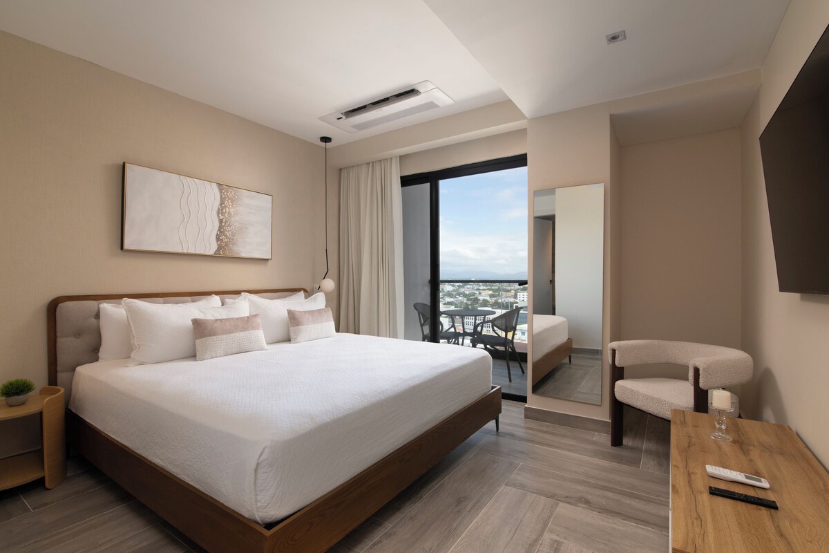 Une chambre d’hôtel moderne avec un grand lit, une petite table, une chaise et une vue sur la ville.