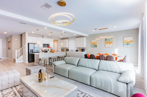 A modern kitchen with white cabinets, a central island, and a dining area with orange chairs.