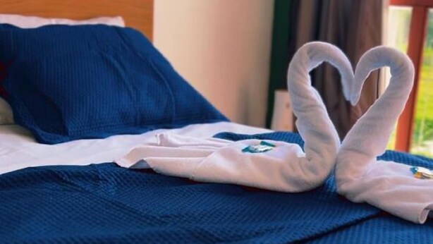A bed with a blue blanket and pillows, and a towel arranged in a heart shape on the bed. - Pedro Alexandre Da Costa (Presidente Figueiredo)
