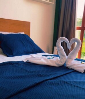 Una cama con una manta azul y almohadas, y una toalla dispuesta en forma de corazón sobre la cama.