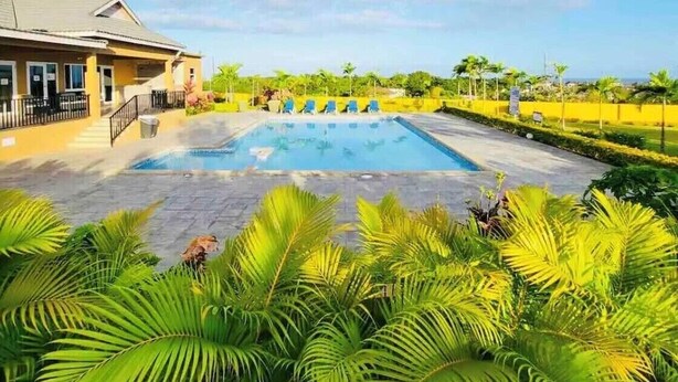 A swimming pool with a sun deck, surrounded by lush greenery and a clear blue sky.