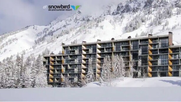 A modern multi-story hotel with a symmetrical facade, large windows, and a snow-covered mountainous backdrop. - Prime ski week studio in enchanting Snowbird (snowbird)