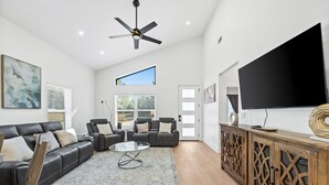 A spacious living room with a black leather sofa, a glass coffee table, and a wooden cabinet with a flat-screen TV. - Modern, Cozy and Spacious Home in Foley Alabama. (Foley)