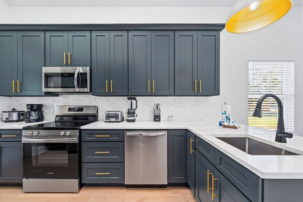 A modern kitchen with dark cabinets, stainless steel appliances, and a white countertop.