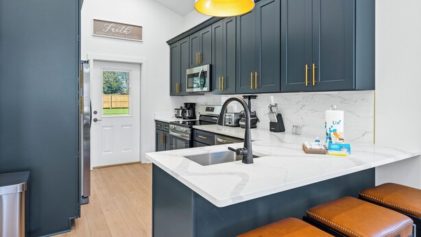 A modern kitchen with dark cabinetry, a white countertop, and a large island with a sink. - Modern, Cozy and Spacious Home in Foley Alabama. (Foley)