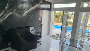 Habitación con sofá de cuero negro, una mesa de vidrio y vistas a una piscina azul exterior.