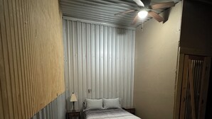 Ett sovrum med en säng, ett nattduksbord, en lampa, en takfläkt och en mönstrad matta.