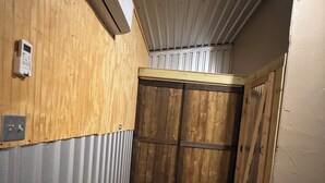 En smal hall med träväggar, en metalldörr och en liten luftkonditioneringsanläggning på väggen.