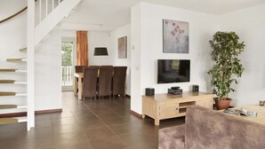 Ein modernes Wohnzimmer mit Treppe, Essbereich, Flachbildfernseher, einer großen Topfpflanze und einer Holzeinrichtung.