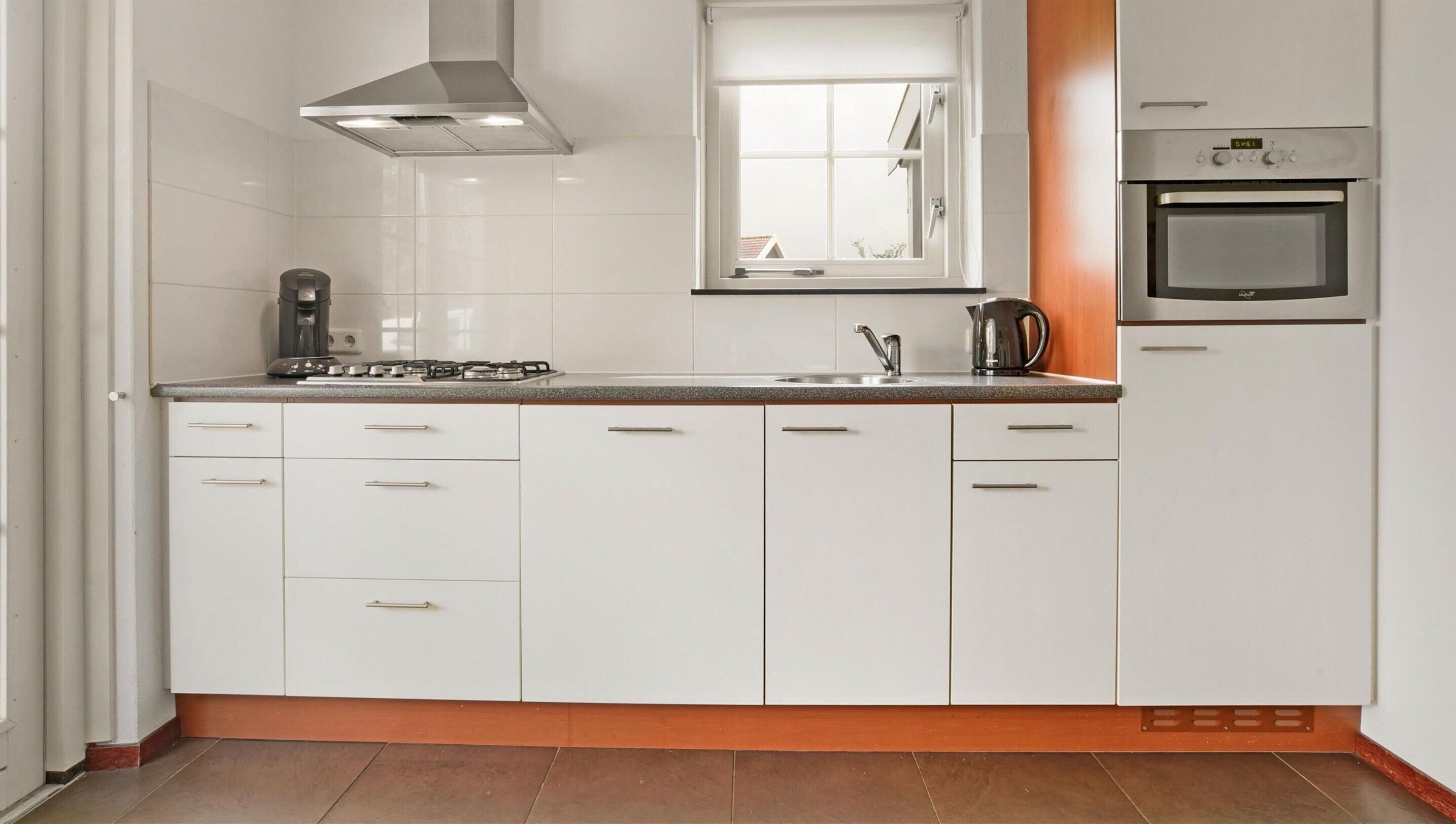 A kitchen with white cabinets, a gas stove, a coffee maker, and a built-in oven.