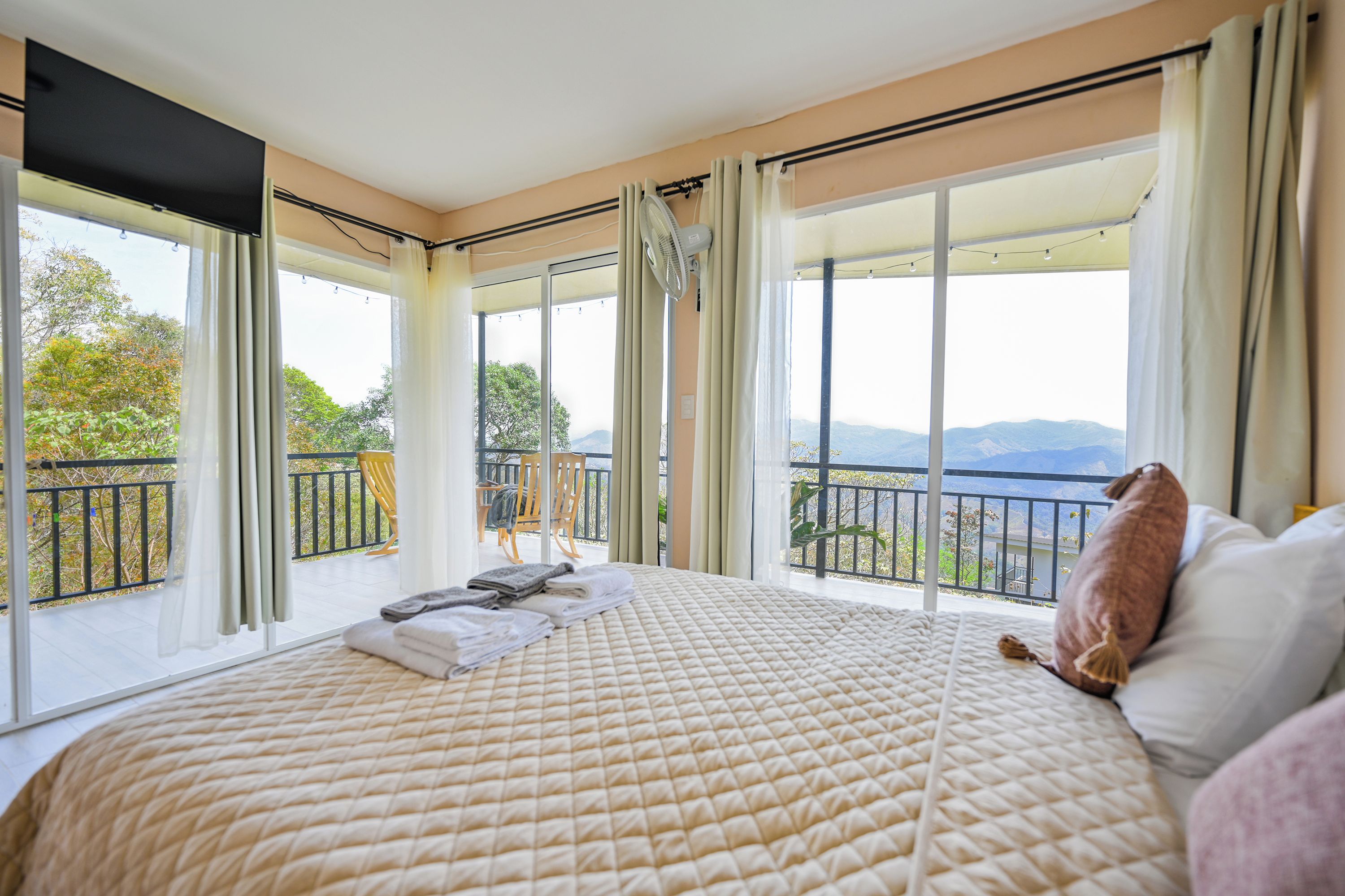 A bedroom with a large bed, a balcony with a view, and a window with curtains.