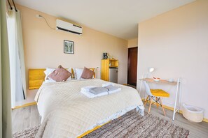 Een hotelkamer met een bed, bureau, stoel, airconditioning en een schilderij aan de muur.