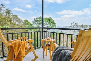 Um deck de madeira com duas cadeiras e uma mesa, com vista para uma paisagem natural.