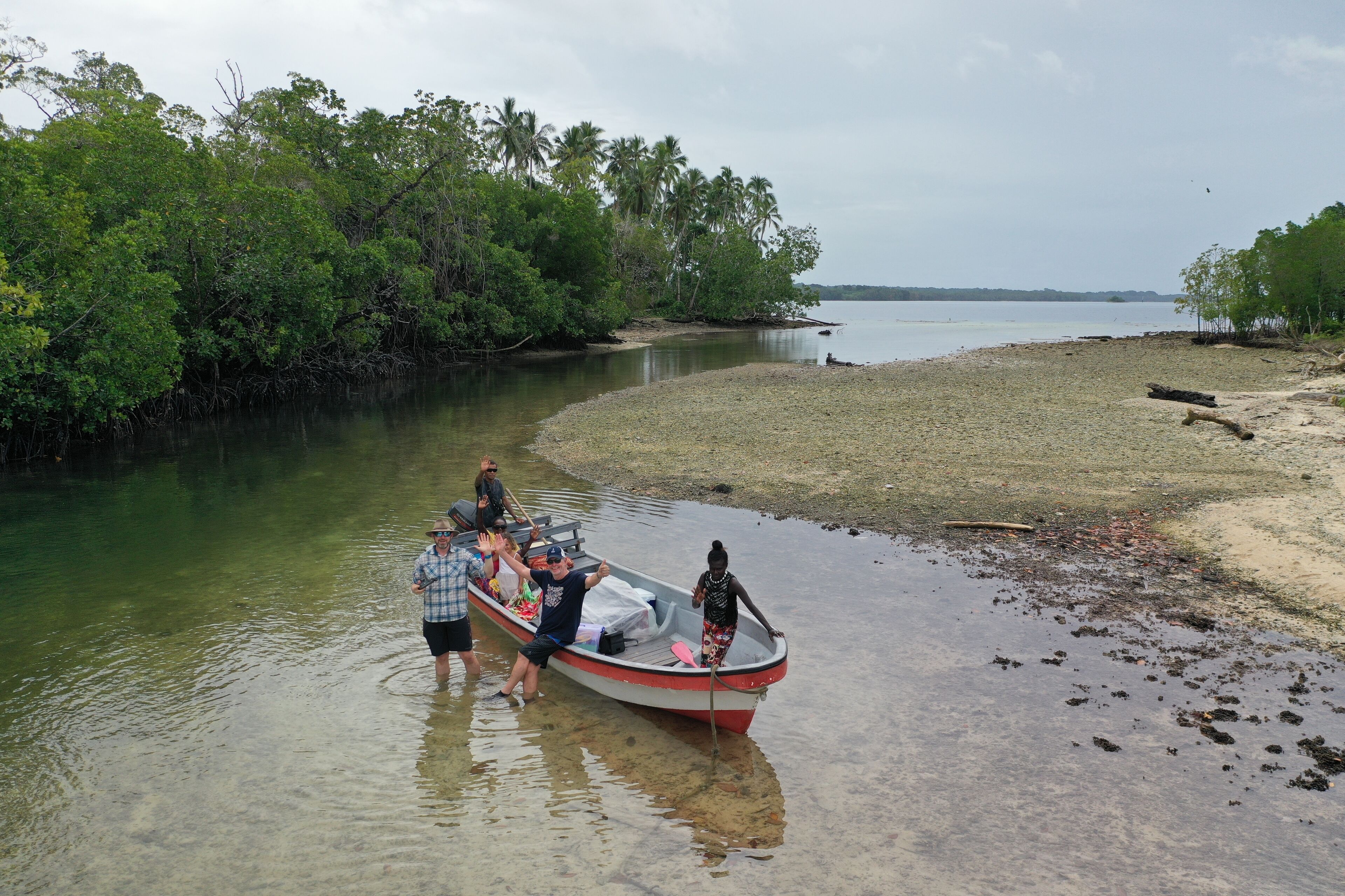 A boat with passengers near a calm riverbank, surrounded by dense greenery.