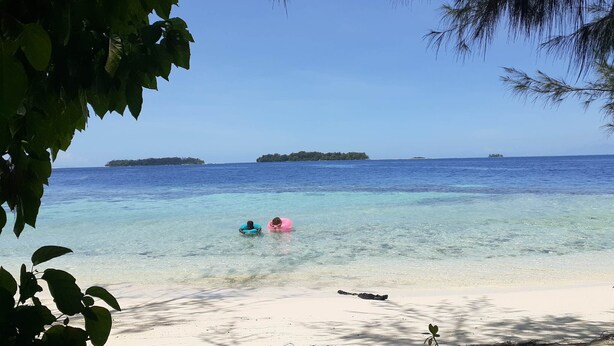 Una playa con agua turquesa cristalina, una orilla arenosa y islas a lo lejos.