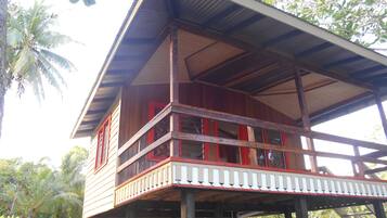 A wooden house with a balcony, surrounded by tropical vegetation.