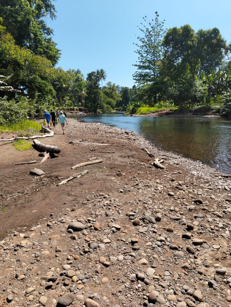 Margem de rio com trilha pedregosa e pessoas caminhando.