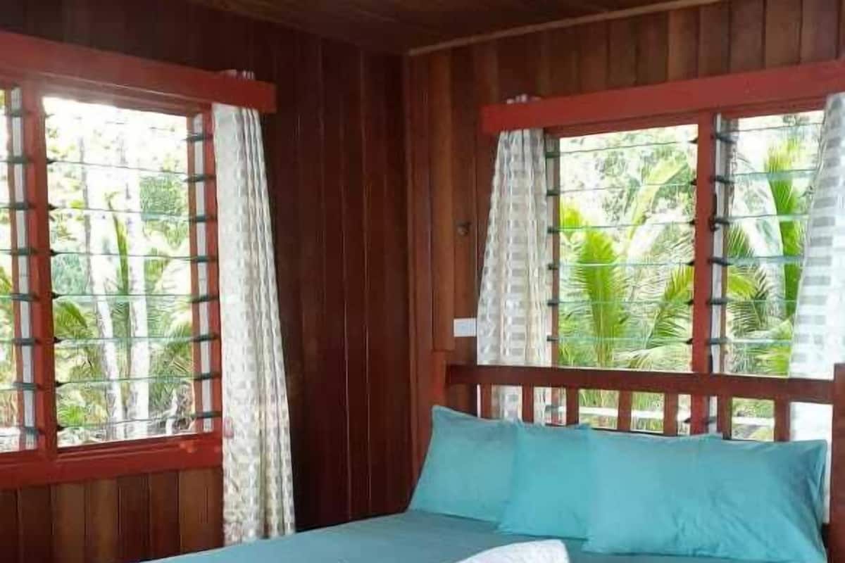 Ein Zimmer aus Holz mit Bett, Vorhängen und einem Fenster.