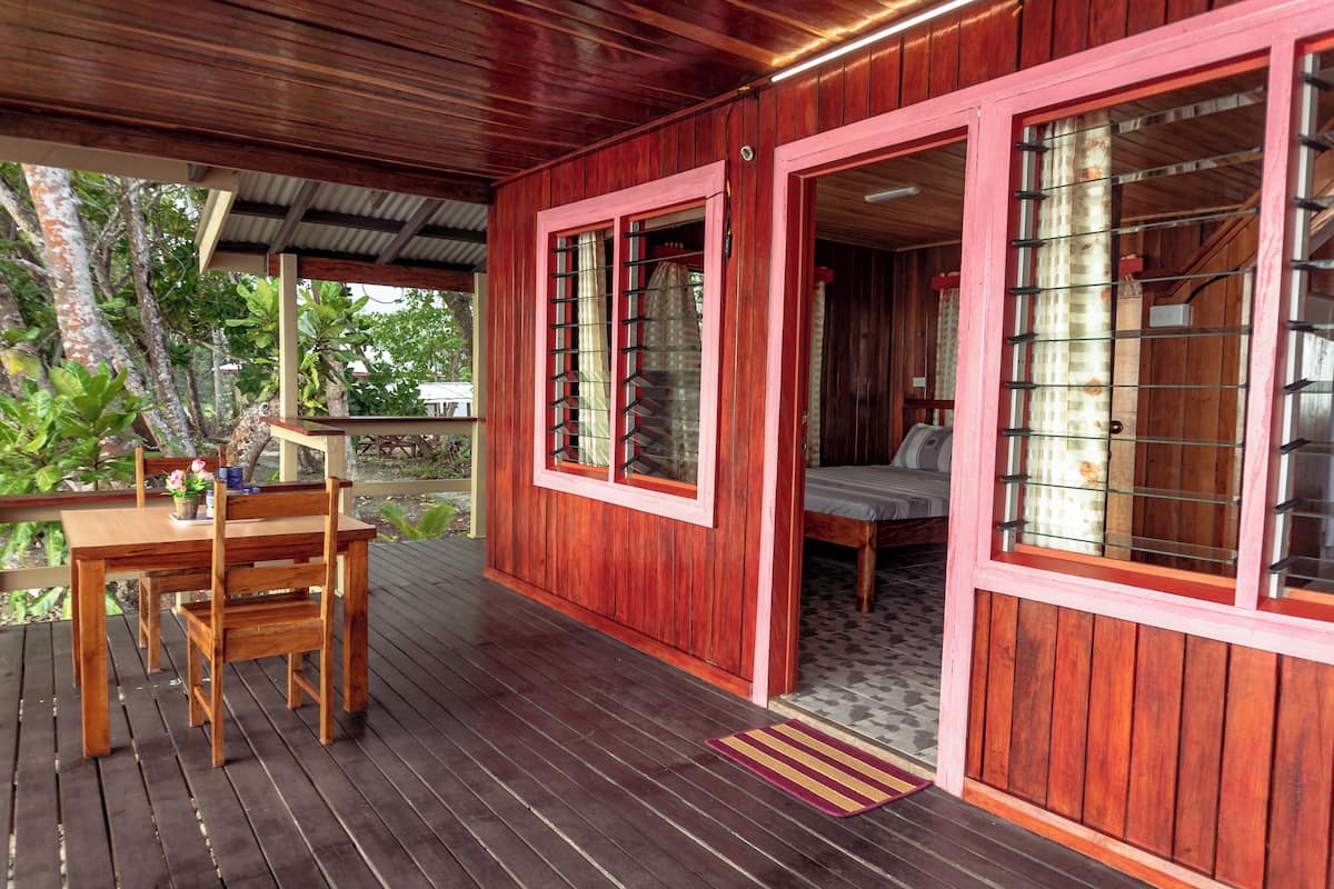 Eine Holzterrasse mit Tisch und Stühlen, ein Bett mit Fenster und ein überdachter Bereich mit Tür.