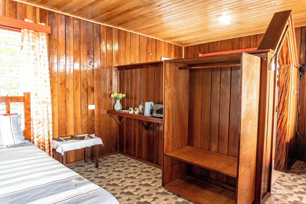 A wooden room with a bed, a table with a vase of flowers, and a bench.