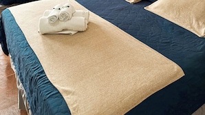 Habitación de hotel con dos camas, cada una con colcha azul y beige, y un juego de toallas sobre la primera cama.