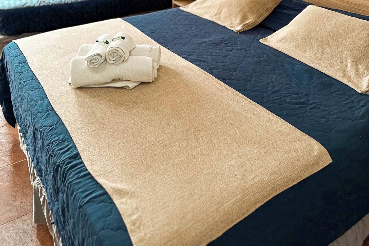 Une chambre d’hôtel avec deux lits, chacun recouvert d’une couverture bleue et beige, et un ensemble de serviettes posé sur le premier lit.
