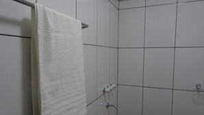 Un baño con azulejos blancos, una toalla colgada en un perchero y una ducha con accesorios cromados.