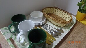Una bandeja con tazas verdes y blancas, tazas blancas, un juego de cucharas doradas y una cesta tejida.