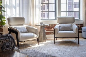 A room with two leather armchairs, a small round table, and a view of a brick building through a window.