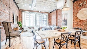Une pièce spacieuse avec une grande table en bois, plusieurs chaises, un canapé et un mur en briques.