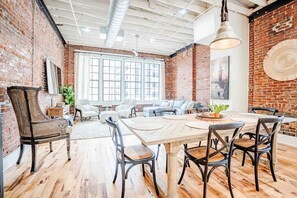 A spacious room with a large wooden table, several chairs, a sofa, and a brick wall. - Modern Stylish & Spacious Loft w/Indoor Parking (Birmingham)