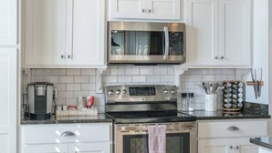Une cuisine moderne avec des meubles blancs, un four à micro-ondes en acier inoxydable, une machine à café et une cuisinière.