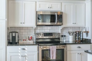 A modern kitchen with white cabinetry, a stainless steel microwave, a coffee maker, and a stove. - Modern Stylish & Spacious Loft w/Indoor Parking (Birmingham)