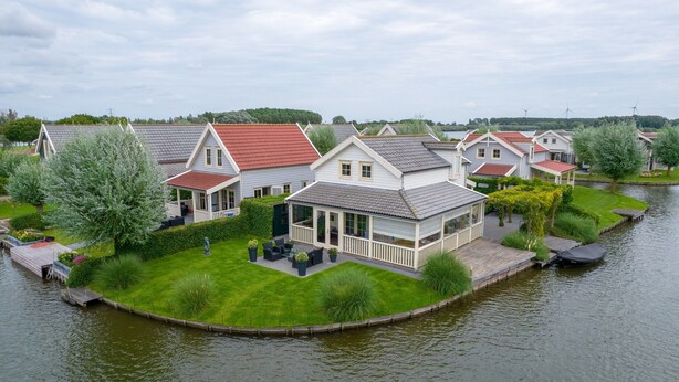 Een rij huizen met een rivier op de voorgrond, met een gazon en een terras.