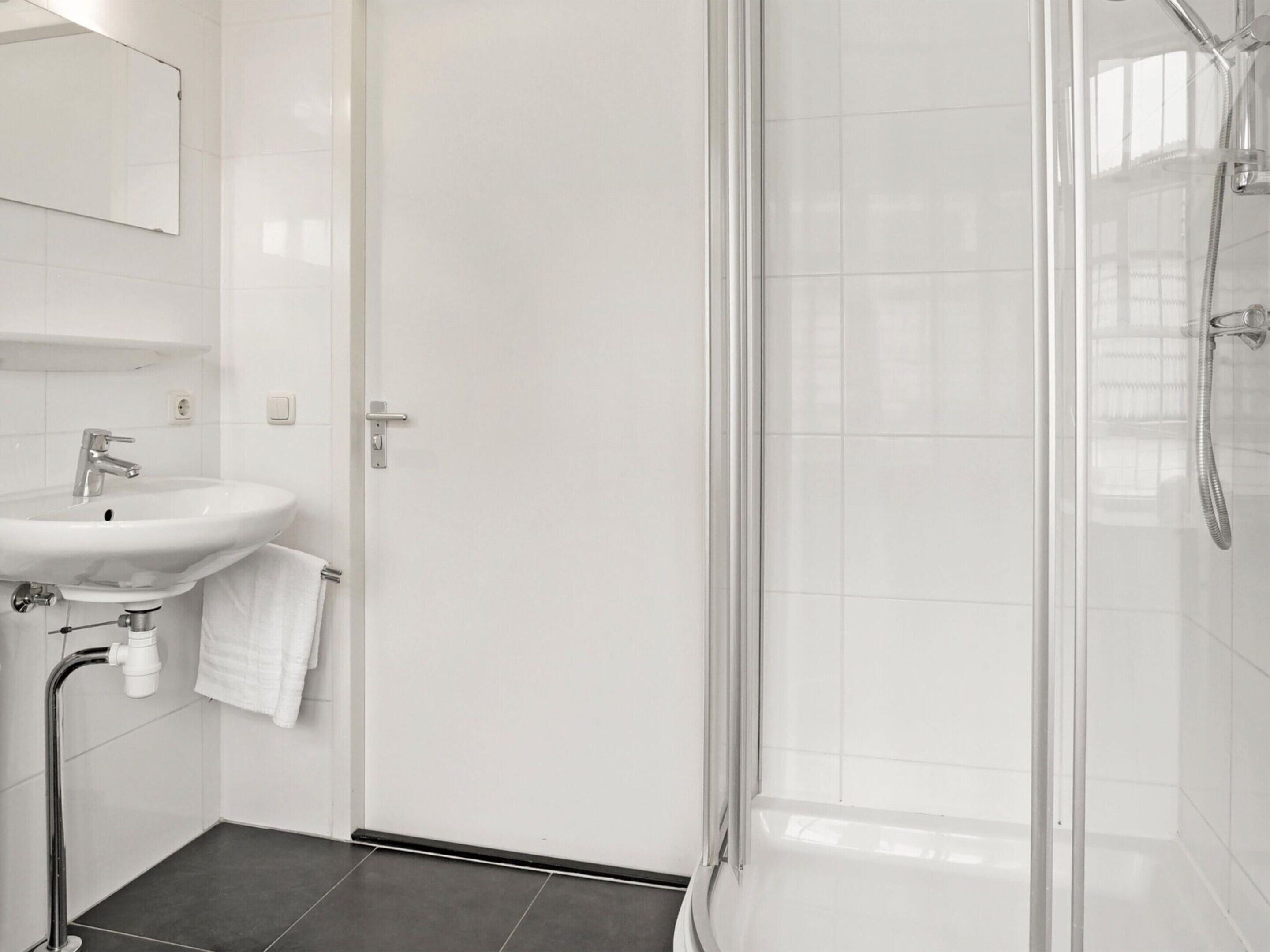 Un baño moderno con lavamanos, espejo y ducha blancos.