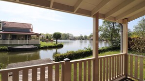 Een overdekt terras met uitzicht op een meer, een huis en een boot.