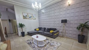 A living room with a sectional sofa, a coffee table, a chandelier, and a patterned rug. - Luxury Lagos House with 4 Bedrooms (Lagos)
