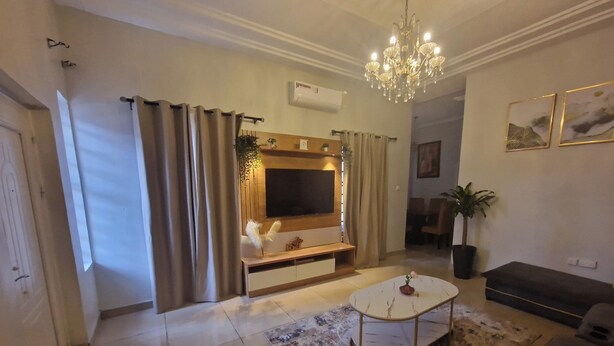 A modern living room with a flat-screen TV, a chandelier, a sofa, and a coffee table. - Luxury Lagos House with 4 Bedrooms (Lagos)