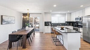 Una cucina moderna con mobili bianchi, una grande isola centrale e un'area pranzo con tavolo e sedie in legno.