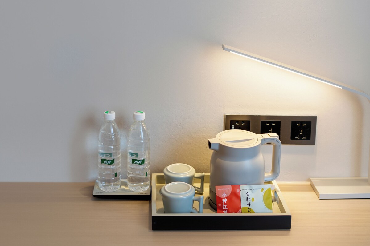 A hotel room with a tray table holding a coffee maker, two cups, and two water bottles.