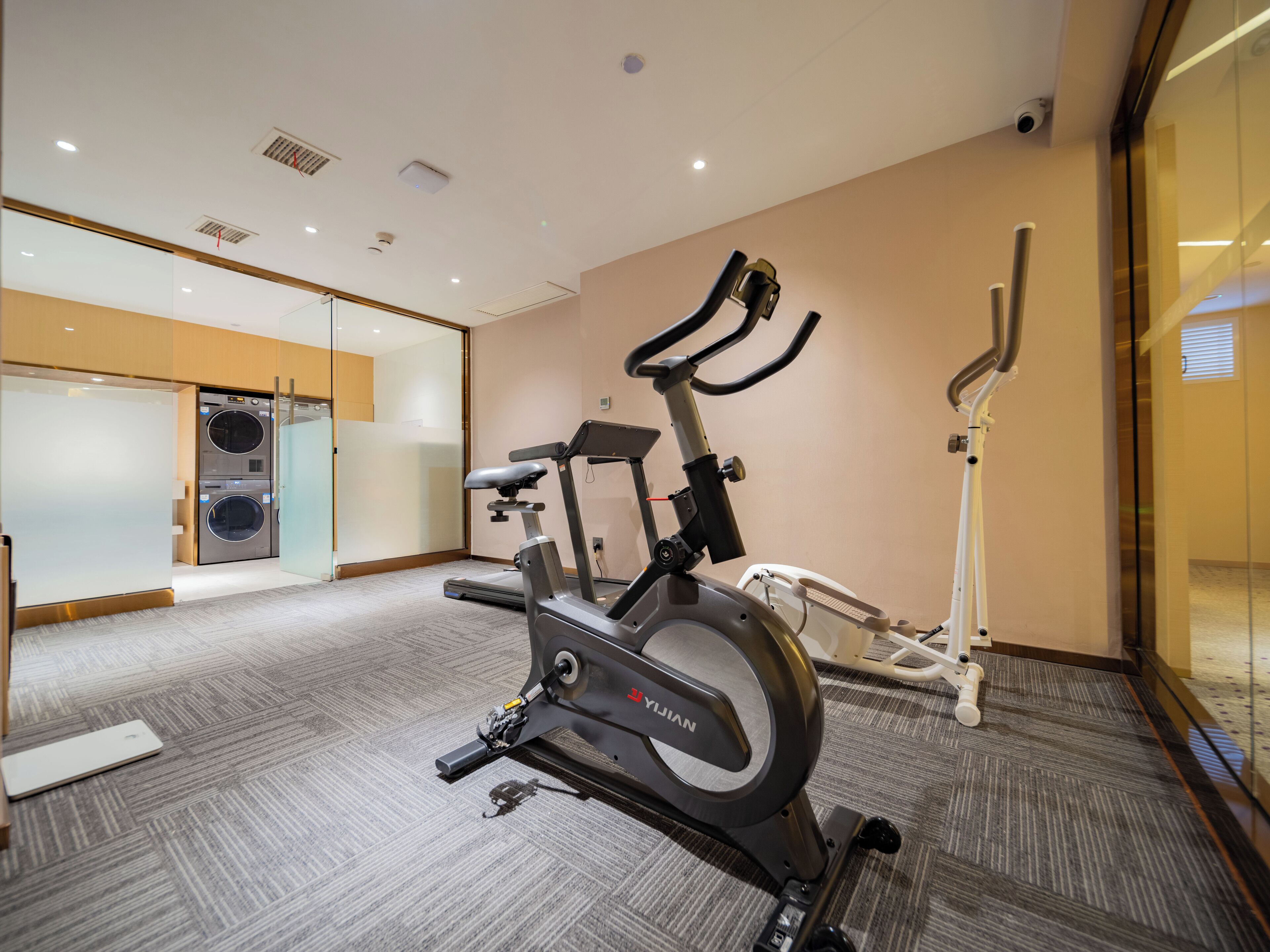 A modern fitness room with a stationary bike, a treadmill, and a wall-mounted elliptical.